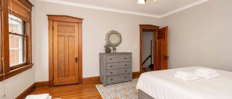 A bedroom with a bed, a dresser, a mirror, a ceiling fan, and a door leading to another room.