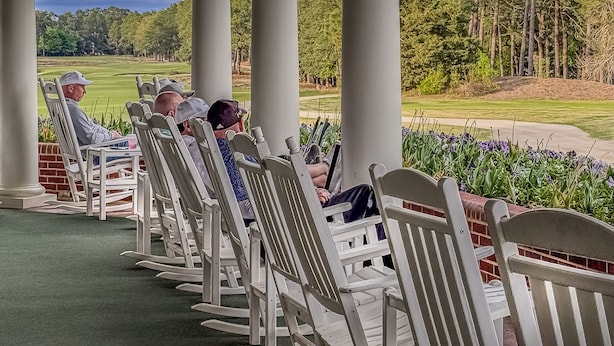 Een overdekt zitgedeelte met witte stoelen en uitzicht op een golfbaan.