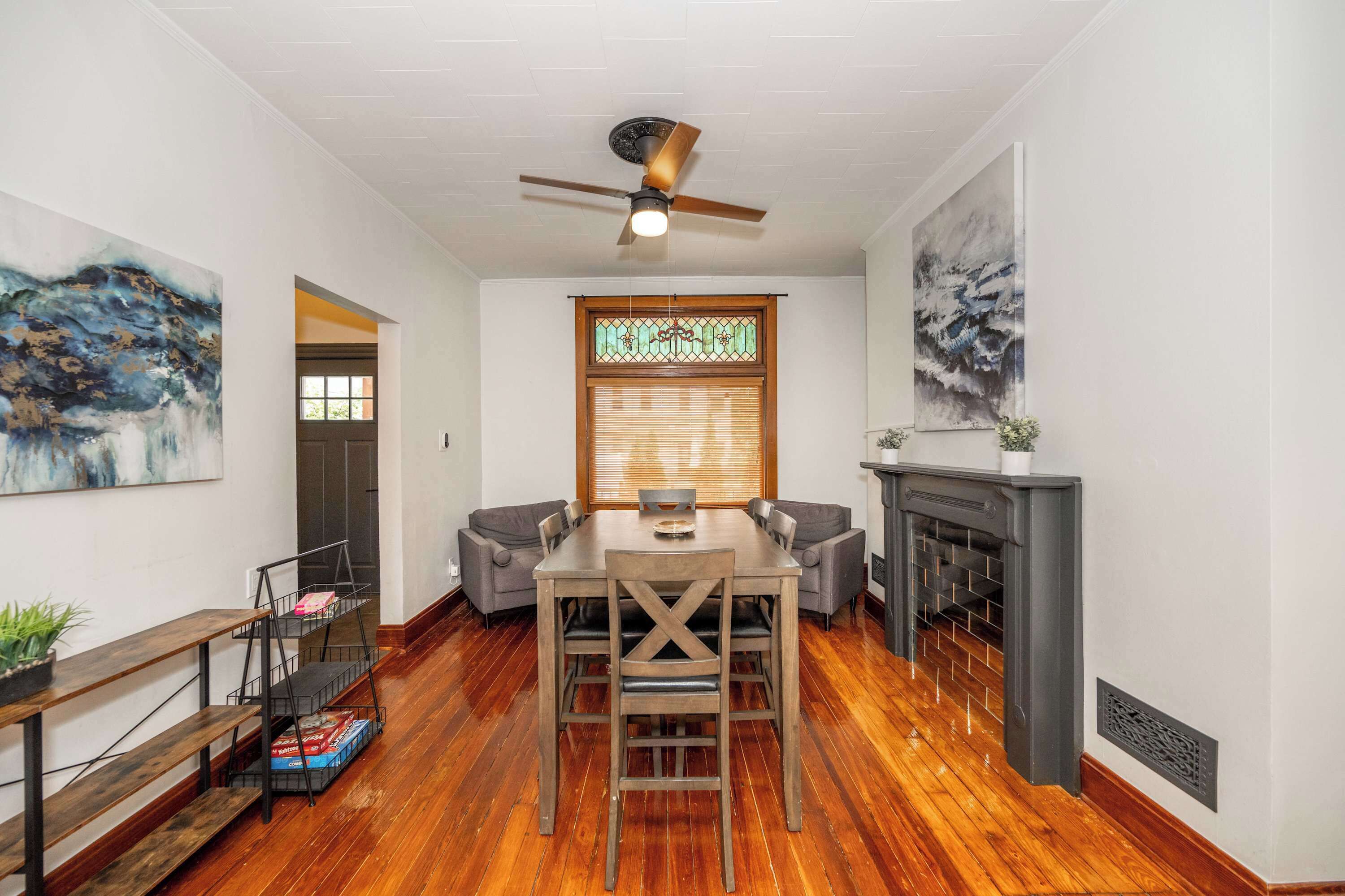 A dining area with a wooden table and chairs, a ceiling fan, a stained glass window, and a fireplace.