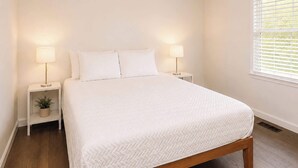 A bedroom with a bed, two bedside tables with lamps, a window with blinds, and a potted plant on one of the nightstands. - Lark Meadow Retreat Sleeps 10! (Mason)
