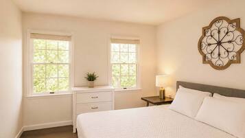 A bedroom with a large bed, two bedside tables, a nightstand, and a decorative wall piece.
