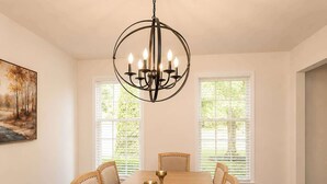 A dining room with a large wooden table, six chairs, a chandelier, and two windows with blinds. - Lark Meadow Retreat Sleeps 10! (Mason)