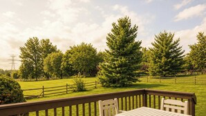 A wooden deck with a table and chairs, overlooking a grassy area with trees and a fence. - Lark Meadow Retreat Sleeps 10! (Mason)