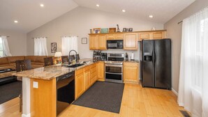 A kitchen with wooden cabinets, a granite countertop, stainless steel appliances, and a dining area with a brown leather couch. - Lazy Days Waterfront for 12! (Williamstown)