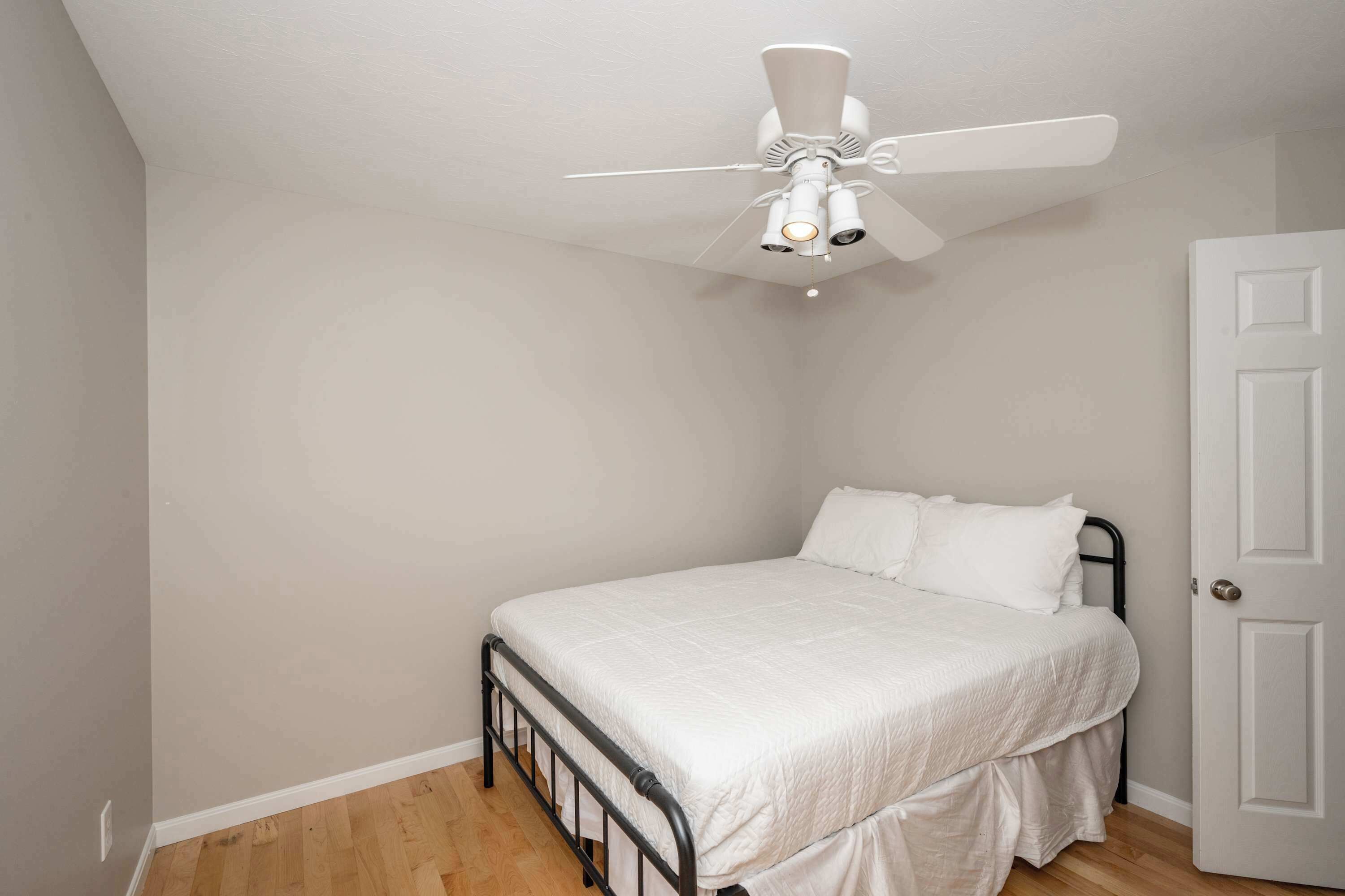 A bedroom with a single bed, a ceiling fan, and a white door.