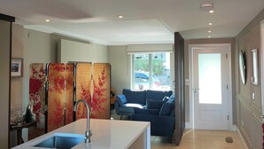A modern kitchen with a central island, a dining area with a blue sofa, and a view of the street outside. - Cozy City Escape in Galway (Galway)