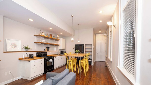 A modern kitchen with white cabinets, a wooden countertop, and a dining area with yellow chairs. - Loft Life Pendleton 2 Chic Downtown Condo for 4! (Cincinnati)