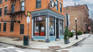 A corner building with a brick facade, a fire escape, and a storefront with a neon sign. - Loft Life Pendleton 2 Chic Downtown Condo for 4! (Cincinnati)