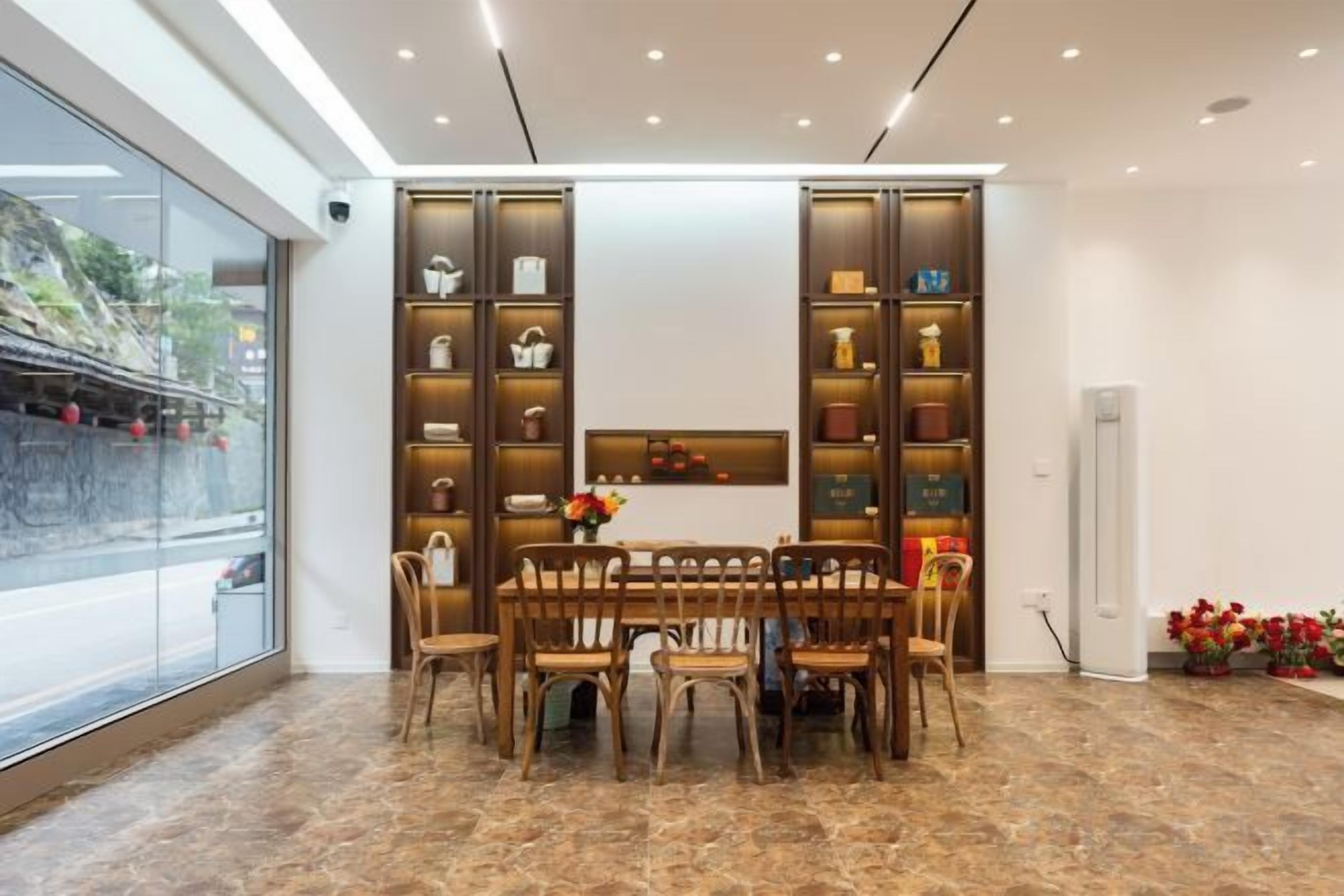 A dining area with a marble floor, a wooden table, and chairs, surrounded by shelves with various items.