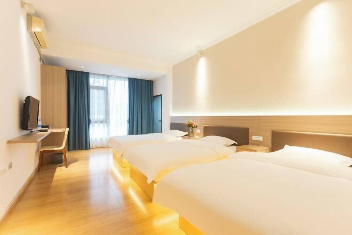 Habitación de hotel con dos camas, un escritorio, un televisor y un ventanal grande con cortinas.