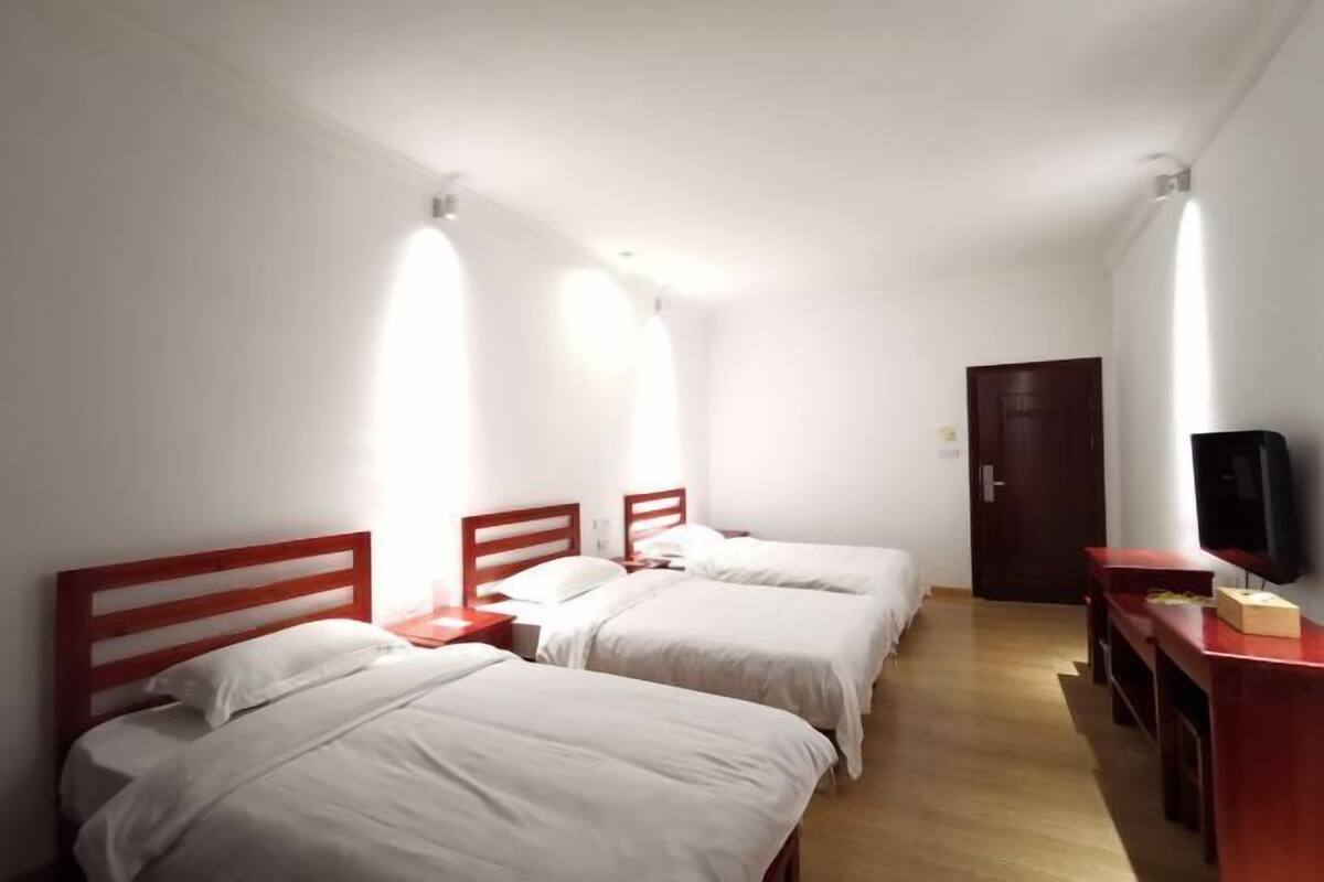 Una habitación con tres camas, un escritorio de madera, televisión y una puerta.