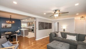 A modern living room with a gray sectional sofa, a wooden floor, a dining area with a dark table, and a kitchen in the background. - Love n Life Haven (Cincinnati)