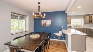 A modern kitchen with a dining area, featuring a wooden dining table, chairs, a chandelier, and a kitchen island. - Love n Life Haven (Cincinnati)