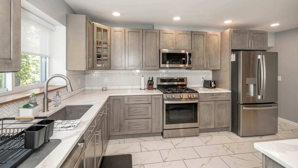 A modern kitchen with grey cabinets, stainless steel appliances, and a herringbone tile backsplash. - Love n Life Haven (Cincinnati)