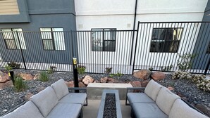 Ein Patio mit zwei grauen Sofas und einem rechteckigen Tisch, umgeben von einem Metallzaun und einem Kiesweg.