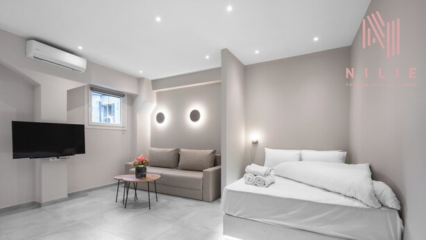 A modern hotel room with a flat-screen TV, a sofa, a small table with a vase, and a neatly made bed. - Bitola, Nilie Hospitality MGMT (Thessaloniki)