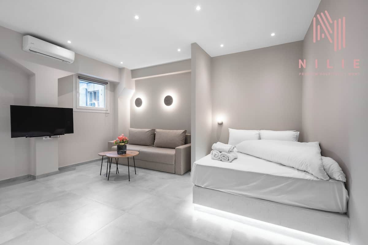 Een moderne hotelkamer met een flatscreen televisie, een bank, een klein tafeltje met een vaas en een netjes opgemaakt bed.