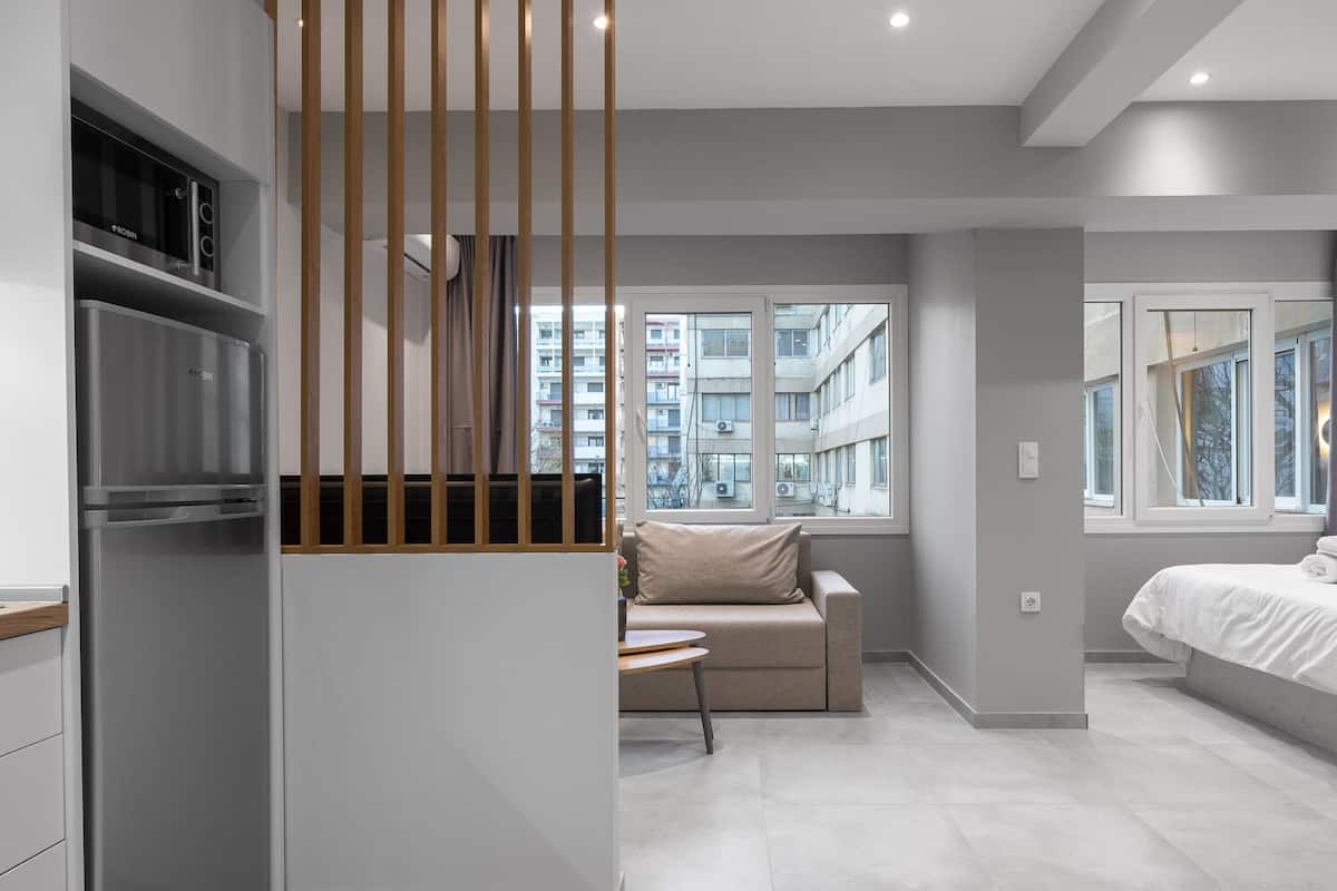 Een moderne, minimalistisch ingerichte slaapkamer met een bed, een sofa en een keukenhoek met een inbouwoven.