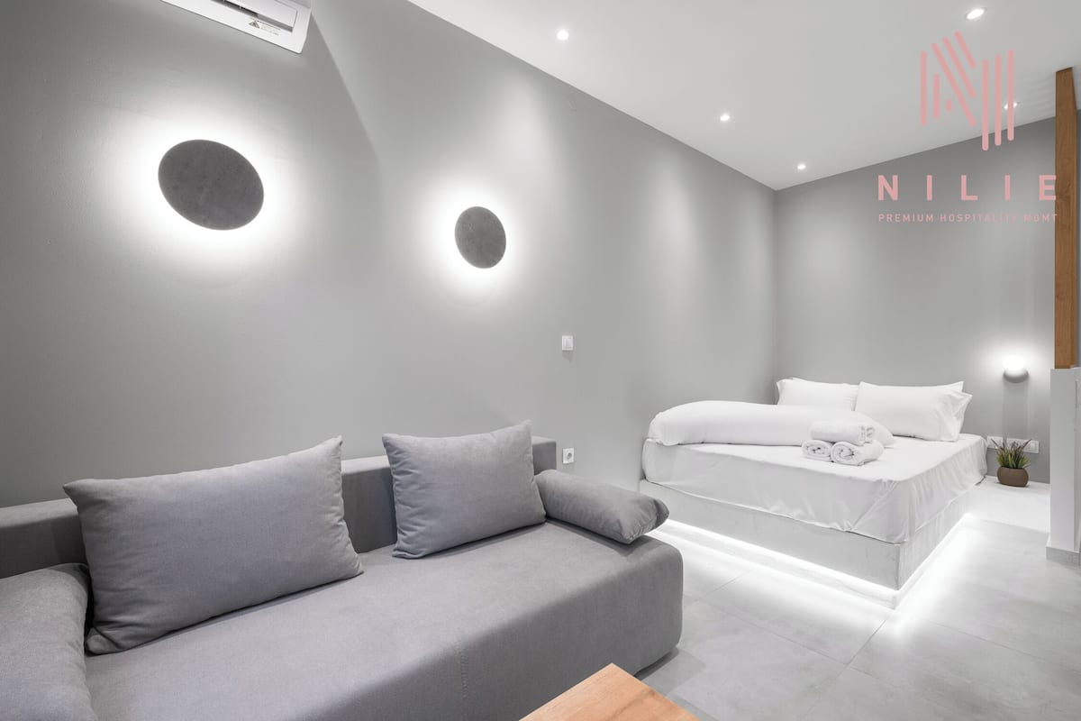 Een moderne hotelkamer met een grijze bank, een net opgemaakt bed en inbouwspots.
