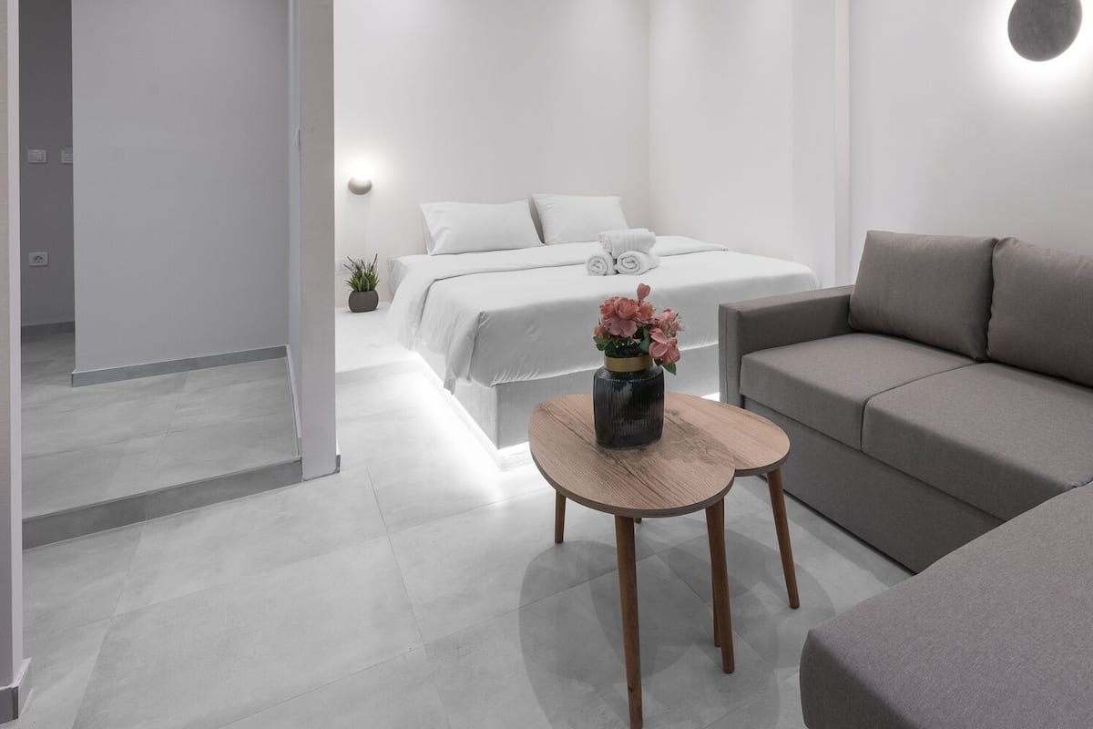 Een moderne hotelkamer met een grijze bank, een klein rond houten tafeltje en een bed met witte lakens.