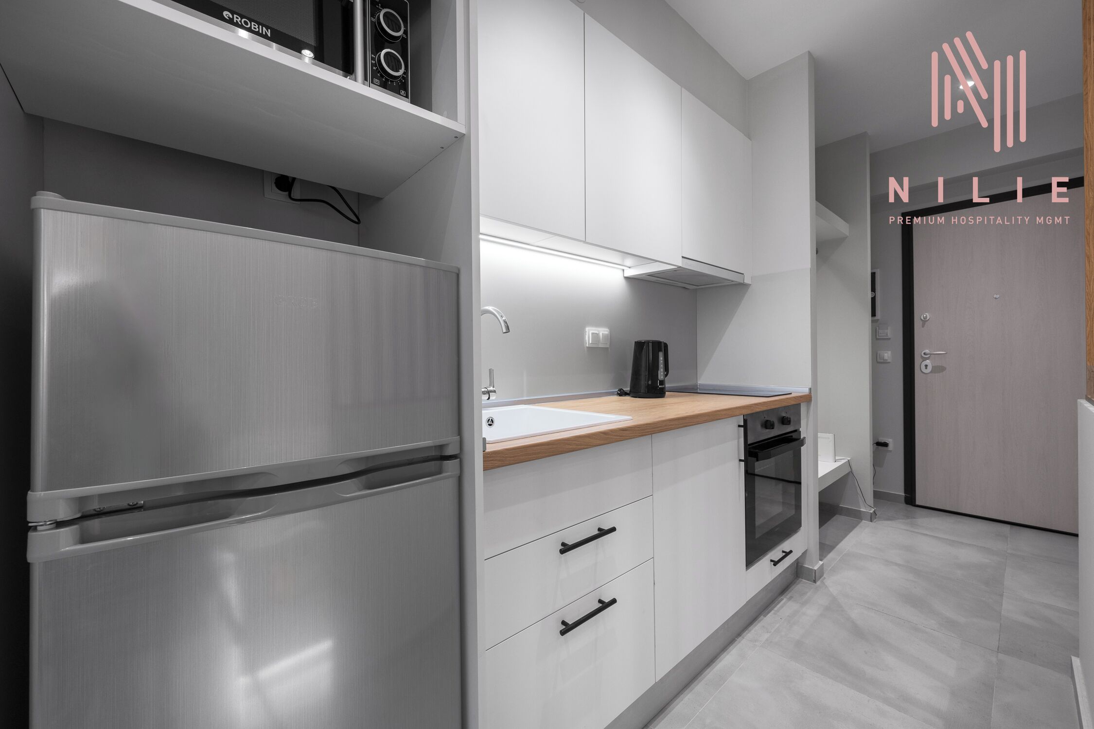 A modern kitchen with stainless steel appliances, white cabinetry, and a wooden countertop.