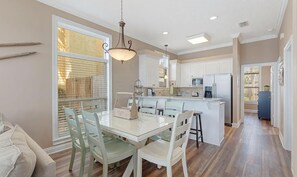 A modern kitchen with white cabinets, a central island, and a dining area with a glass table and chairs. - Turquoise Tail (Panama City Beach)