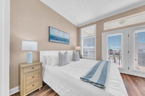 A bedroom with a bed, nightstands, a painting, and a view through the window. - Turquoise Tail (Panama City Beach)