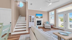 A spacious living room with a staircase, a fireplace, and a large window with blinds. - Turquoise Tail (Panama City Beach)