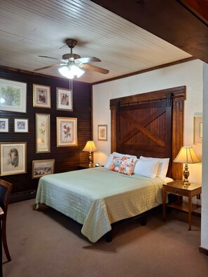 A bedroom with a bed, two bedside tables with lamps, a ceiling fan, and a barn-style door. - Inn at Lake Joseph (Forestburgh)