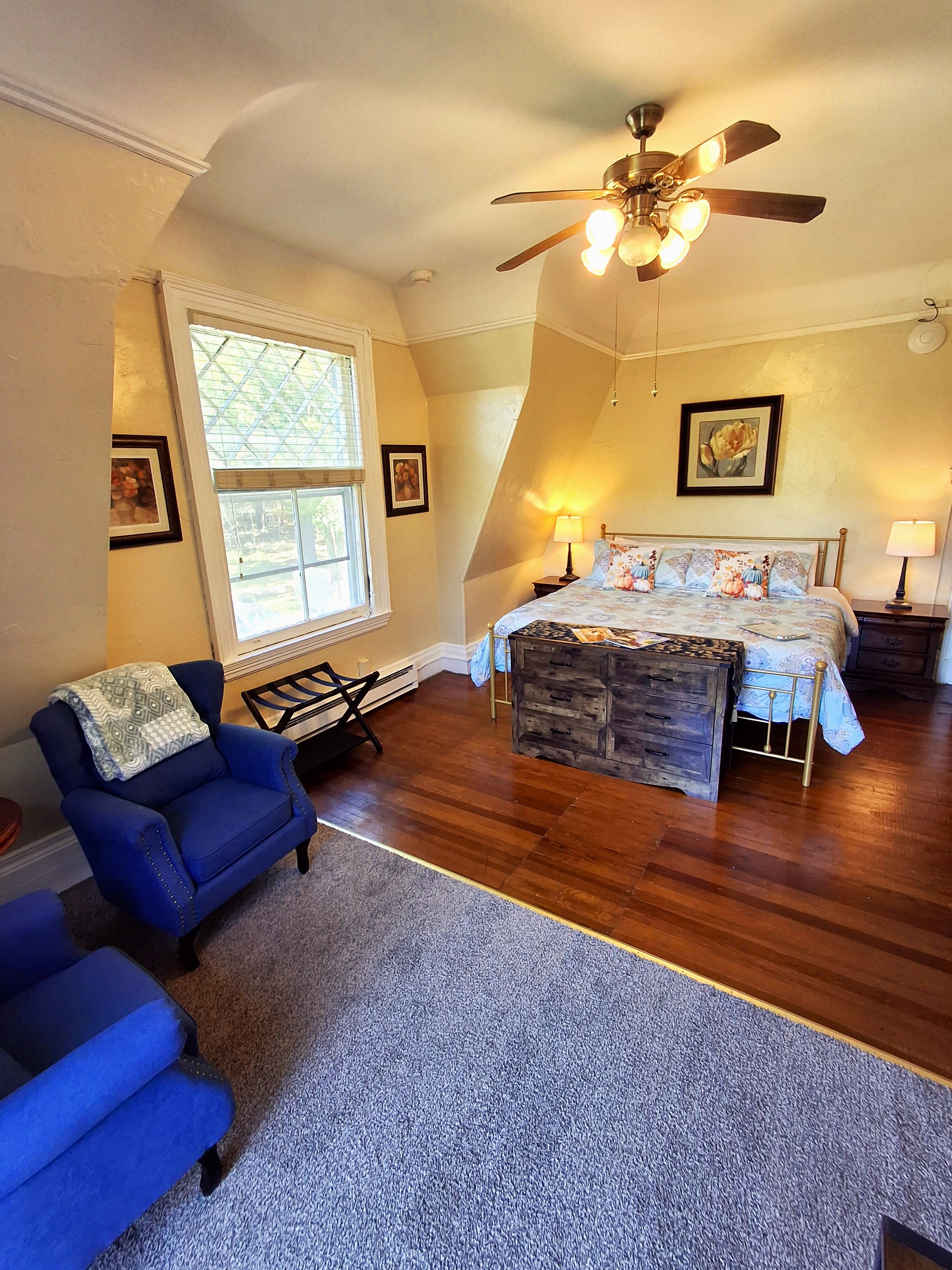 A bedroom with a bed, a chair, a ceiling fan, and a window.