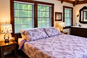 A bedroom with a bed, two bedside lamps, a nightstand, a dresser, a mirror, and a window with blinds.
