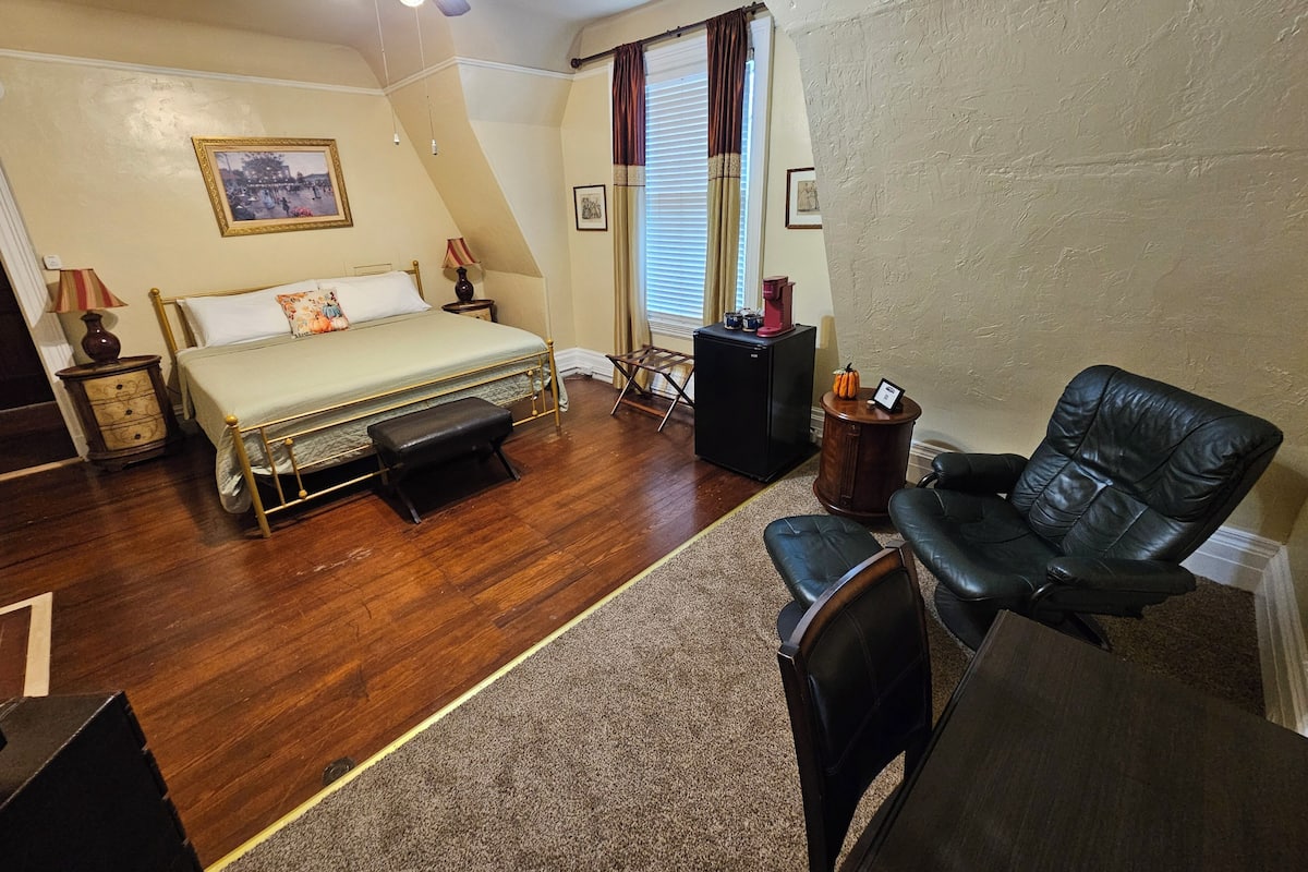 A bedroom with a bed, a desk, a chair, a ceiling fan, and a window with curtains.