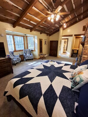 Un dormitorio con una cama grande, ventilador de techo, vigas de madera y vistas al exterior.