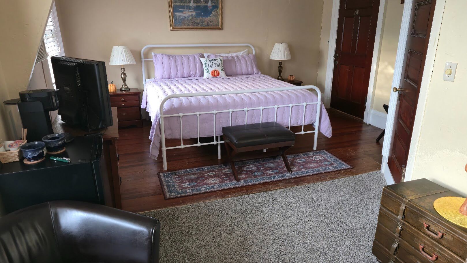 A bedroom with a bed, bedside lamps, a television, a desk, and a dresser.