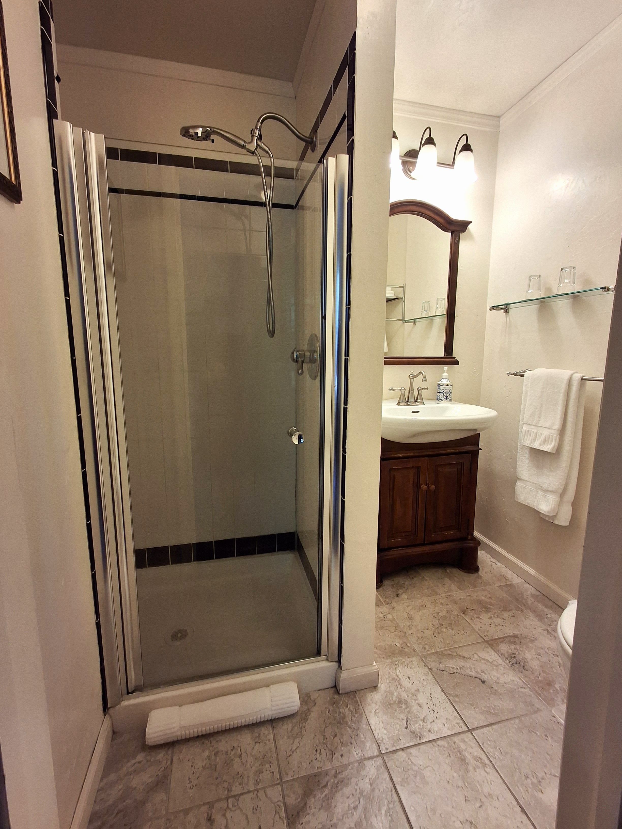 A modern bathroom with a glass-enclosed shower, a vanity with a mirror, and a towel rack.