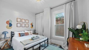 Un dormitorio con cama, mesita de noche, lámpara y ventana con cortinas.