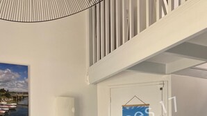 A modern interior with a grey sofa, a white door with a view of a blue sky and buildings, and a staircase with wooden steps. - Apartment with Sea View Oléron LesTerrasses17 - 28 (Saint-Pierre-d'Oléron)