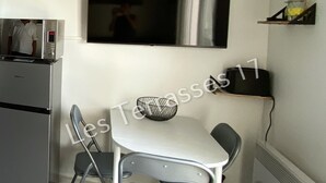 A compact kitchen with a microwave, a small refrigerator, a white table with two chairs, and a flat-screen TV mounted on the wall. - Apartment with Sea View Oléron LesTerrasses17 - 28 (Saint-Pierre-d'Oléron)