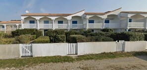 A row of white buildings with balconies, a gated entrance, and well-maintained hedges.