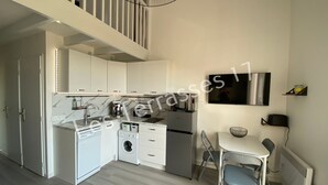 A compact kitchen with white cabinets, a built-in oven, a microwave, and a washing machine. There is a dining area with a table and chairs, and a TV mounted on the wall. - Apartment with Sea View Oléron LesTerrasses17 - 28 (Saint-Pierre-d'Oléron)