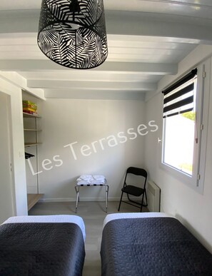 Ein Schlafzimmer mit zwei Betten, einem Heizkörper, einem Sessel, einem Regal mit Kisten und einem Fenster mit Jalousien.