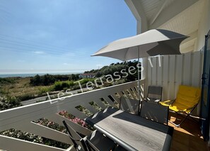 Un balcon avec vue sur la mer, une chaise jaune et un parasol gris.