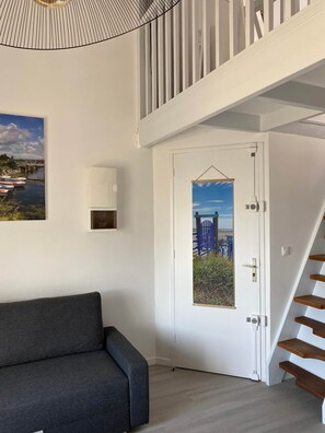 A modern interior with a grey sofa, a white door with a blue gate view, and a staircase with wooden steps.