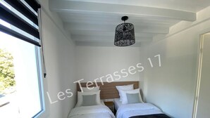 A small, well-lit bedroom with two beds, a wooden headboard, and a hanging light fixture. - Apartment with Sea View Oléron LesTerrasses17 - 28 (Saint-Pierre-d'Oléron)