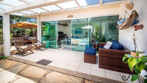A covered patio area with wicker furniture, a glass door leading to a room, and a sign that says "PRAIA".