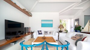 A modern living room with a flat-screen TV, white sofas, a wooden coffee table, and a blue chair.