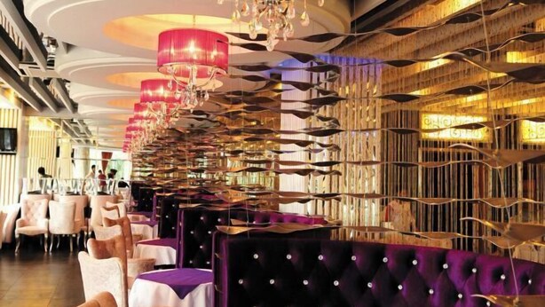 L’intérieur d’un restaurant avec des rangées de sièges en gradin, des lustres et un mur orné de motifs.