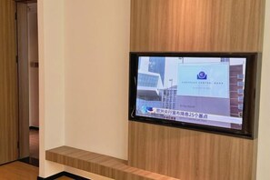 A television mounted on a wall displaying a news broadcast. - Yangguang Yihao Hotel (Qionghai)
