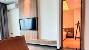 Une chambre d’hôtel moderne dotée d’un téléviseur à écran plat fixé au mur, d’un mur d’accent en bois, d’un lit avec une table de chevet et d’un trépied placé dans un coin.