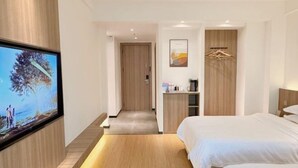 Une chambre d’hôtel moderne avec un téléviseur fixé au mur, un plancher en bois, un lit, un petit bureau et une armoire.